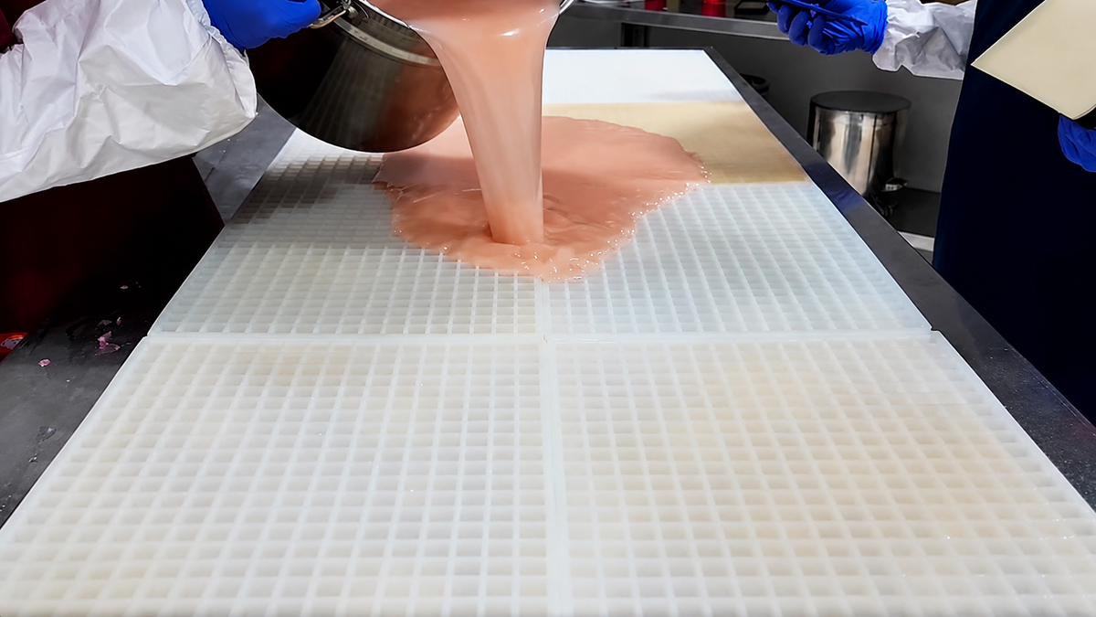 Gummy Molds-team giet gummymengsel over een grote commerciële siliconen mal vóór het afschrapen