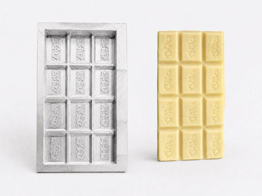 Aluminium prototype met één holte voor chocoladereep naast een afgewerkte witte chocolade testreep