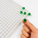 Close-up van een smaragdgroene 1 mL kubusgummy naast de vorm met 736 holtes