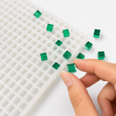 Smaragdgroene 1 mL kubusgummy naast de siliconen vorm met 736 holtes